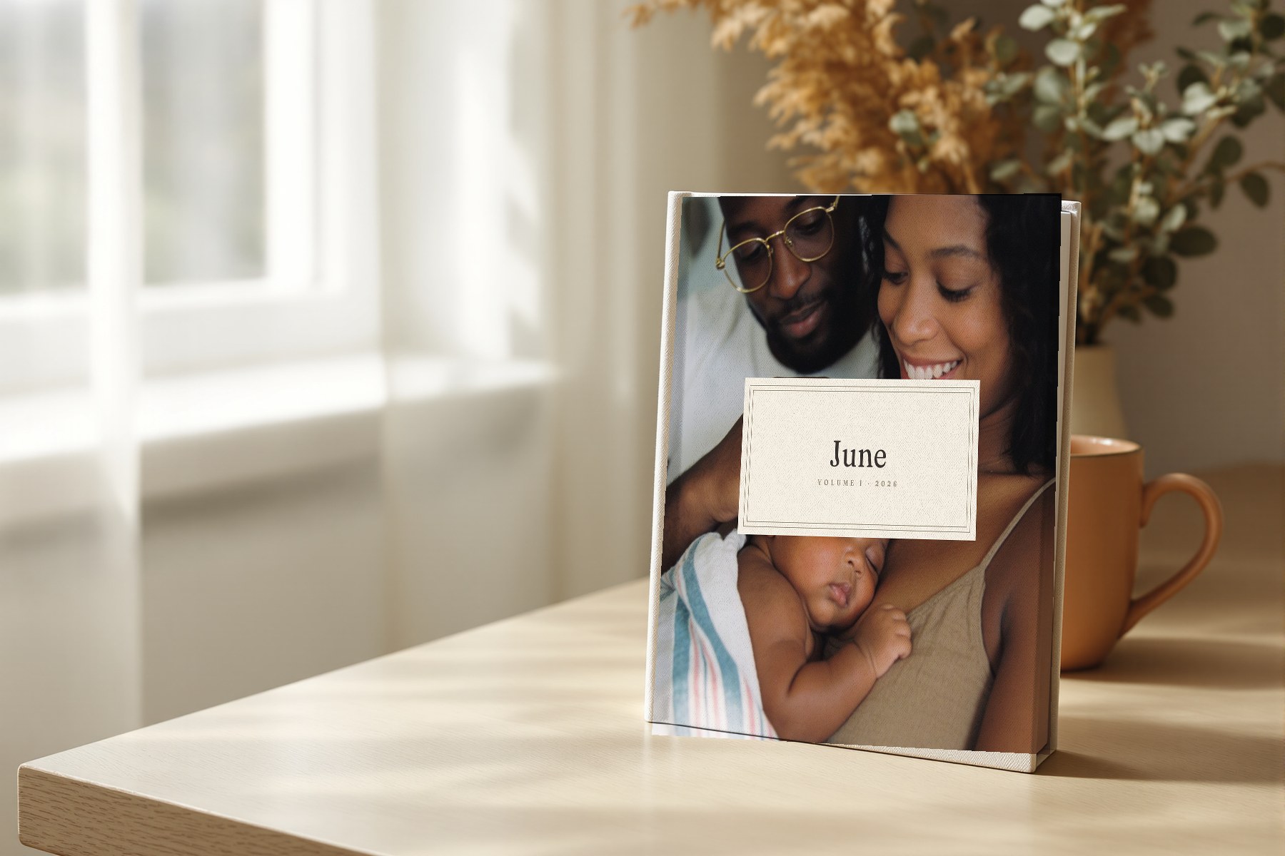 A square linen-bound Volume One baby book standing on an oak table by a window